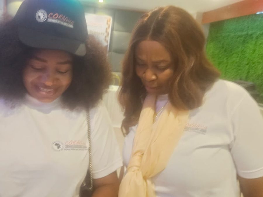 Two women in CORAfrica T-shirts and caps, smiling as they look down