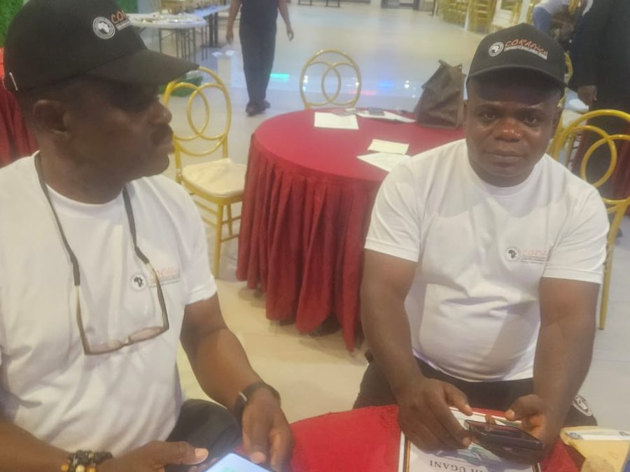 Two men in CORAfrica T-shirts and caps seated at a table