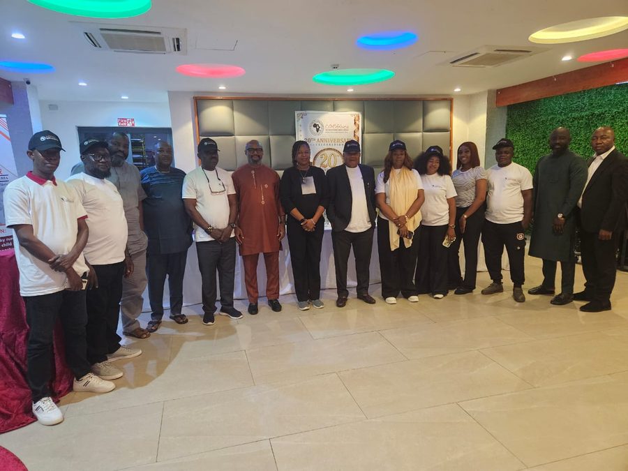 Guests in white CORAfrica T-shirts and caps lined up before the twentieth-anniversary banner at the Abuja celebration