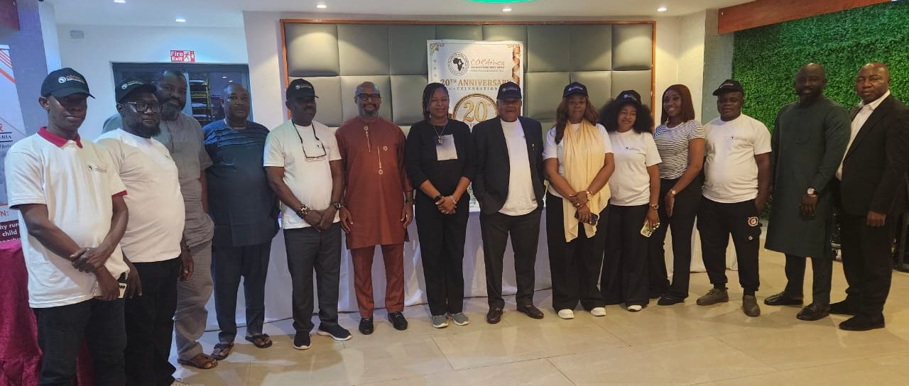 Guests in white CORAfrica T-shirts and caps lined up before the twentieth-anniversary banner
