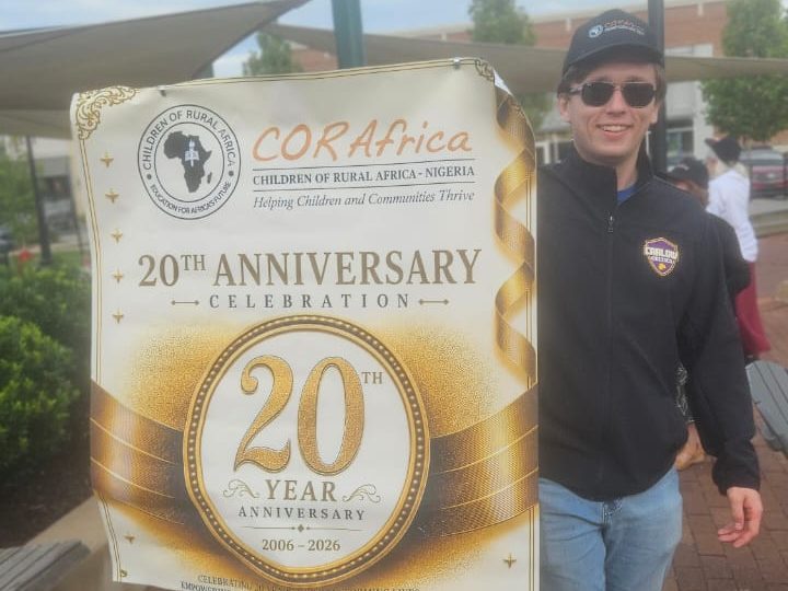 A young man in a CORAfrica cap beside the twentieth-anniversary banner
