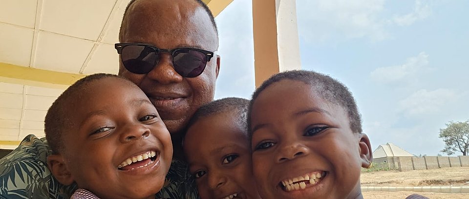 Fr. Peter Abue with three laughing children outside a CORAfrica building